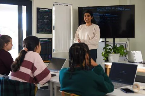 Female teacher leading code class in light sweater with laptops and screen Stock Photos