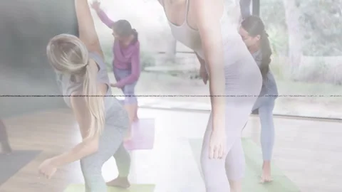 Female teacher reaching down to correct student alignment guiding yoga class Stock Footage 332545328