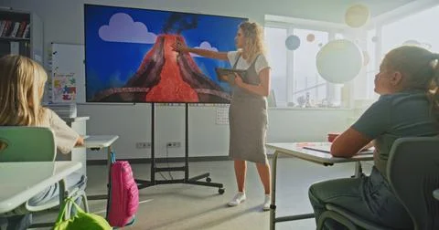 Female Teacher with Tablet Computer Explaining Volcanic Eruption Process to Kids Stock Photos
