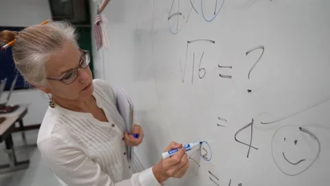 Female teacher writing math equations on a white board in a school room for Stock Footage 137642687