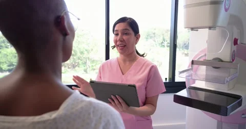 Female tech explaining mammogram to female patient in imaging room using tablet Stock Footage 337705266