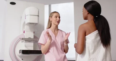 Female tech in pink scrubs gesturing, explaining mammography unit, reassuring Stock Footage 335808888