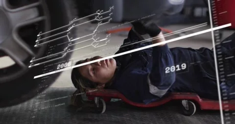 Female tech on red creeper under car dates sliding across wheel lifting head Stock Footage 329910437