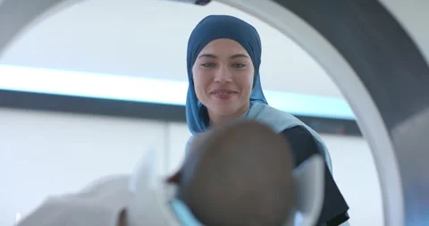Female tech in scrubs ID smiling in scanner ring, checking headrest while table Stock Footage 337537408