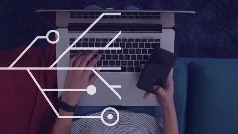 Female tech worker typing on laptop and tilting phone, causing circuit nodes Stock Footage 334465814