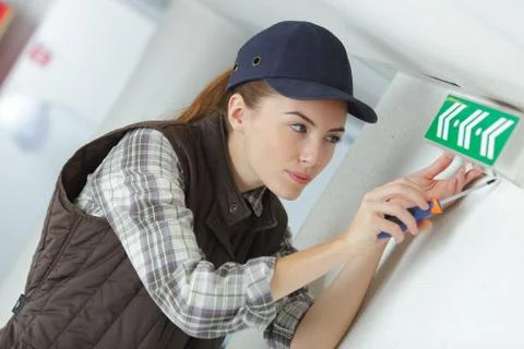 Female technician fitting a fire exit sign Stock Photos