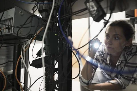 Female technician with flashlight working at server panel in dark server room Foto stock