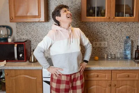 Female throwing head back in laughter while standing in a home kitchen 스톡 사진