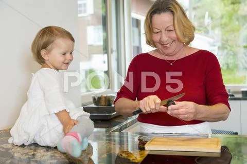 Female Toddler Sitting On Kitchen Counter Watching Grandmother