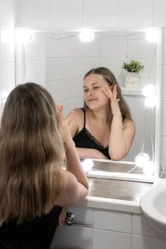 Female touching face while doing self care morning routine in home bathroom with Stock Photos