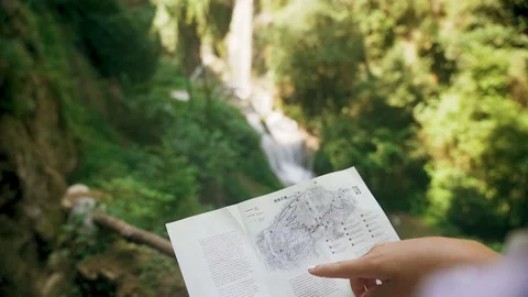 Female tourist with a backpack checking paper map near mountain waterfall Stock Footage 107822187