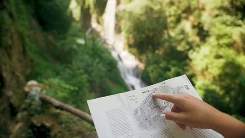 Female tourist with a backpack checking paper map near mountain waterfall Stock Footage 107822419