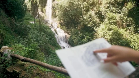 Female tourist with a backpack checking paper map near mountain waterfall Stock Footage 107822636