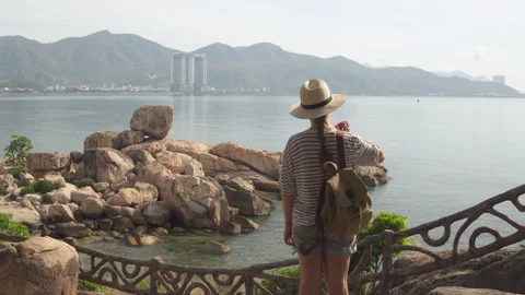 Female tourist in hat puts on backpack. Awesome seascape Stock Footage 320761435