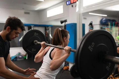 A female trainee lifting weights while being watched by her coach Stock Photos