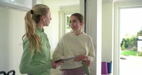 Female trainer and client entering gym holding tablet, sipping from water bottle Stock Footage 341664828