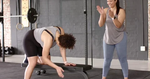 Female trainer and client performing dumbbell rows after cues at gym bench, Stock Footage 340454309