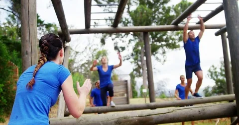 Female trainer clapping hands while fit people climbing monkey bars 4k 動画素材 82243999
