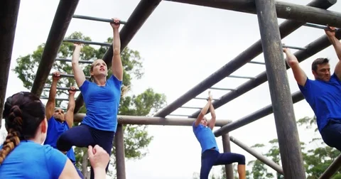 Female trainer clapping hands while fit people climbing monkey bars 4k 動画素材 82244033