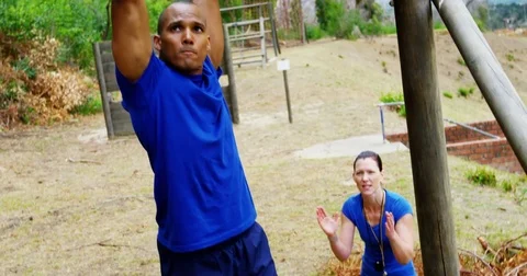 Female trainer clapping hands while fit man climbing monkey bars 4k 動画素材 82244540