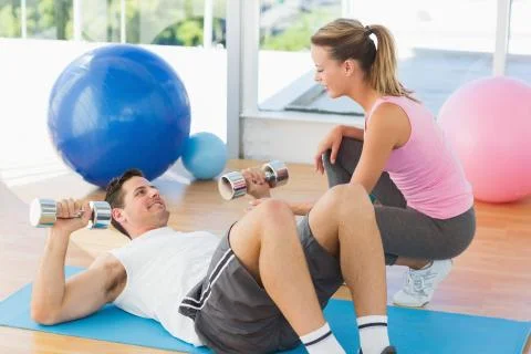 Female trainer looking at young man exercise in gym Stock Photos