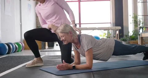 Female trainer in pink touching senior client's back, aligning forearm plank on Stock Footage 342084710