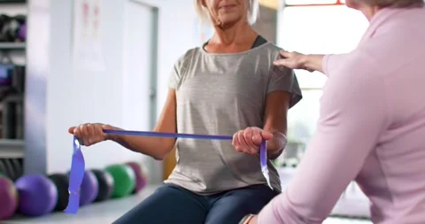 Female trainer placing hand on shoulder, knee, guiding client pulling band on Stock Footage 342032823