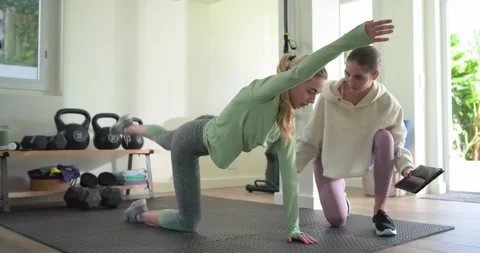 Female trainer using tablet and leading female trainee through bird-dog pose for Stock Footage 336305822