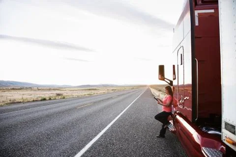 Female truck driver standing next to the cab of her truck near the highway in Stock Photos