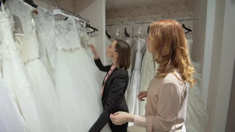 Female trying on wedding dress in a shop with women assistant Stock Footage