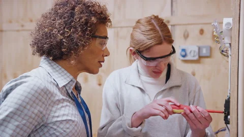 Female Tutor With Trainee Electrician In Workshop Studying For Apprenticeship At Stock Footage 130611296