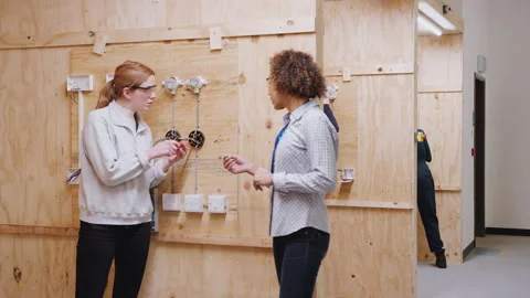 Female Tutor With Trainee Electricians In Workshop Studying For Apprenticeship Stock Footage 130610943