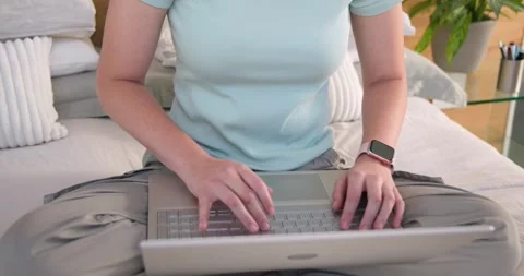 Female typing on laptop while working on bed with smartwatch, camera pulling Stock Footage 340988240