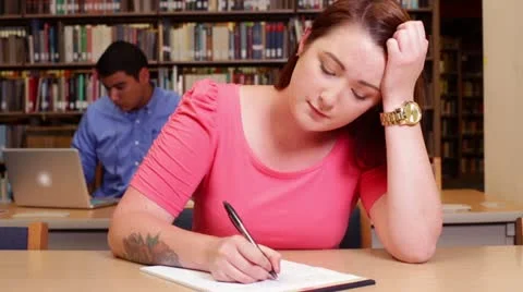 Female university student trying to write in the library Stock Footage 22385308