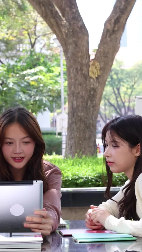 Female University Students Laughing While Studying With Digital Tablet Outdoors 動画素材 335266180