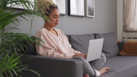 Female using laptop while sitting on comfortable sofa at home Stock Footage 97842440