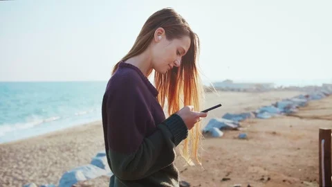 Female using smartphone to text to beloved friend or couple using app on beach Stock Footage 100452354