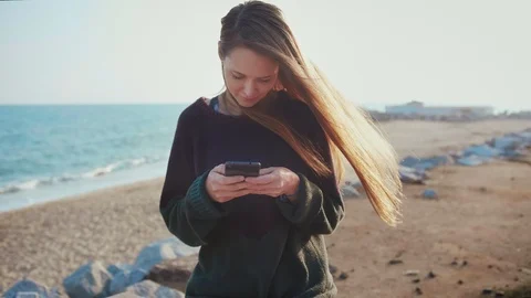 Female using smartphone texting or writing to beloved friend or couple on beach Stock Footage 100452326