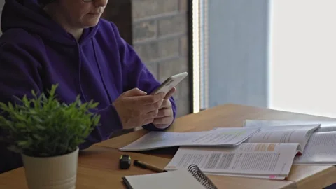 Female using smartphone typing messaging sitting table opened books papers Stock Footage 243268825