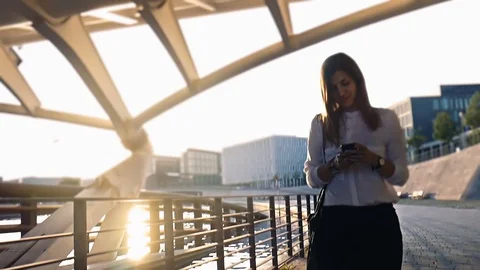Female using smartphone walking on a pedestrian at Sunset Stock-Footage 78726415