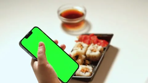 Female using smartphone while eating sushi rolls at home. Green screen Stock Footage 292116956