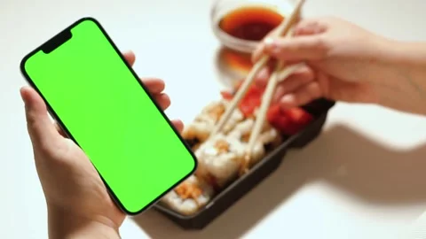 Female using smartphone while eating sushi rolls at home. Green screen Stock Footage 292116957
