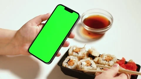 Female using smartphone while eating sushi rolls at home. Green screen Stock Footage 293195627