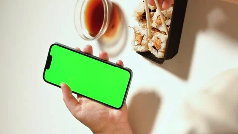 Female using smartphone while eating sushi rolls at home. Green screen Stock Footage 293195648