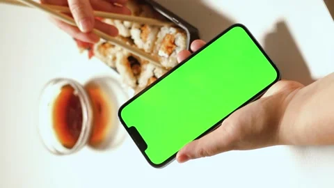 Female using smartphone while eating sushi rolls at home. Green screen Stock Footage 293919091
