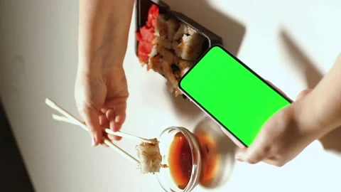 Female using smartphone while eating sushi rolls at home. Green screen Stock Footage 293919180