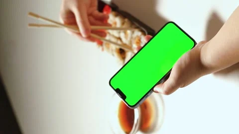 Female using smartphone while eating sushi rolls at home. Green screen Stock Footage 295115327