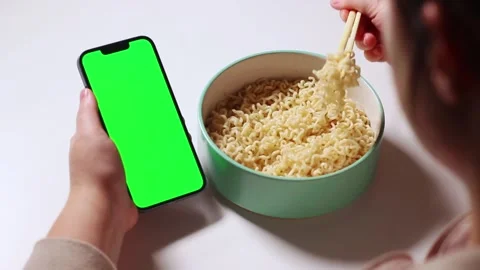 Female using smartphone while eating pasta at home. Green screen Stock Footage 295140996