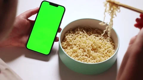 Female using smartphone while eating pasta at home. Smartphone with green Stock Footage 304900250
