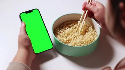 Female using smartphone while eating pasta at home. Smartphone with green Stock Footage 304900251